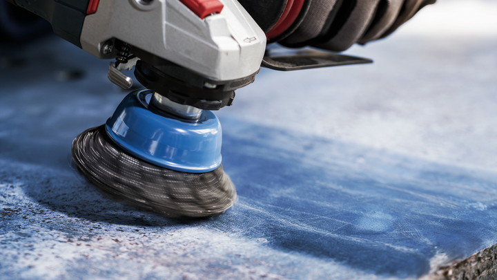 บุคคลที่สวมอุปกรณ์ด้านความปลอดภัยกำลังขัดพื้นหินสีน้ำเงินด้วยแปรงถ้วยลวด