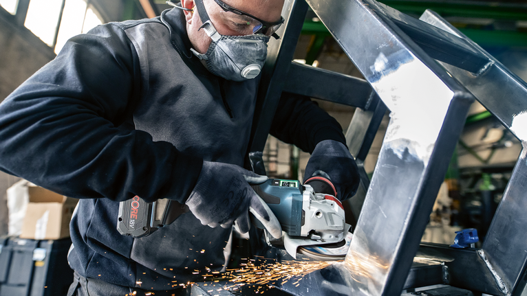 บุคคลที่สวมอุปกรณ์ความปลอดภัยทำการเจียรโครงโลหะ ทำให้เกิดประกายไฟ