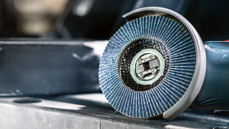 ภาพระยะใกล้ของเครื่องเจียรจานขัดสีน้ำเงินที่วางอยู่บนพื้นผิวโลหะ