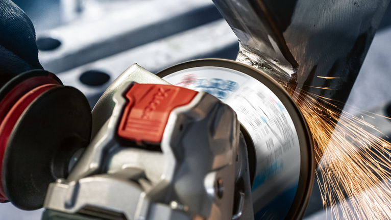 บุคคลที่สวมอุปกรณ์ความปลอดภัยกำลังเจียรโลหะ ทำให้เกิดประกายไฟด้วยเครื่องเจียรแบบมุม