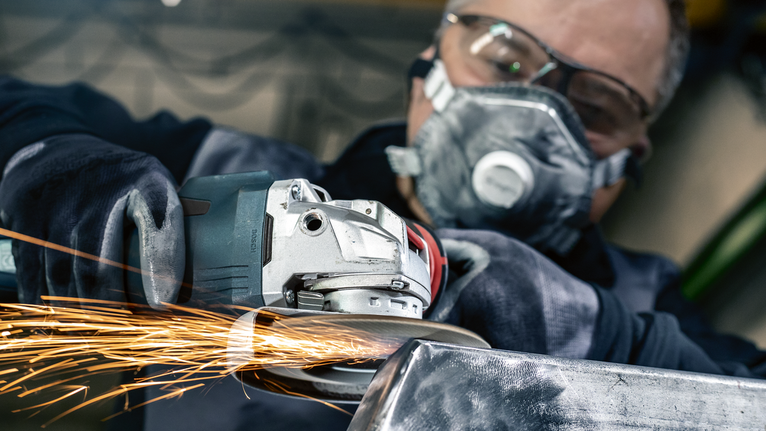 บุคคลที่สวมอุปกรณ์ความปลอดภัยกำลังบดโลหะ ทำให้เกิดประกายไฟที่สว่าง