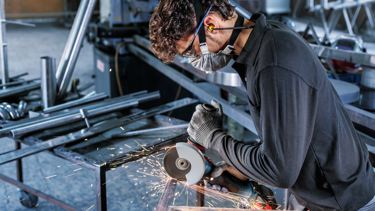 บุคคลที่สวมอุปกรณ์ความปลอดภัยใช้เครื่องเจียรตัดโลหะ จึงเกิดประกายไฟขึ้น