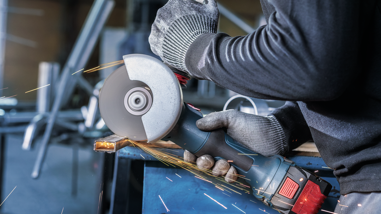 บุคคลที่สวมอุปกรณ์ความปลอดภัยทำการบดโลหะ ทำให้เกิดประกายไฟ