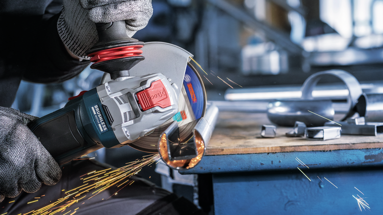 บุคคลที่สวมอุปกรณ์ความปลอดภัยกำลังบดท่อโลหะ ทำให้เกิดประกายไฟ