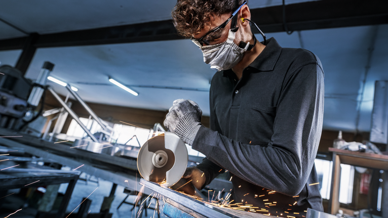 ผู้ที่สวมอุปกรณ์นิรภัยตัดโลหะด้วยเครื่องเจียร มีประกายไฟกระเด็นออกมา