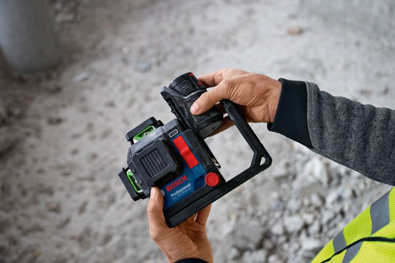 บุคคลที่สวมอุปกรณ์ความปลอดภัยถือเครื่องมือวัดระดับเลเซอร์พร้อมแบตเตอรี่ที่ติดอยู่.