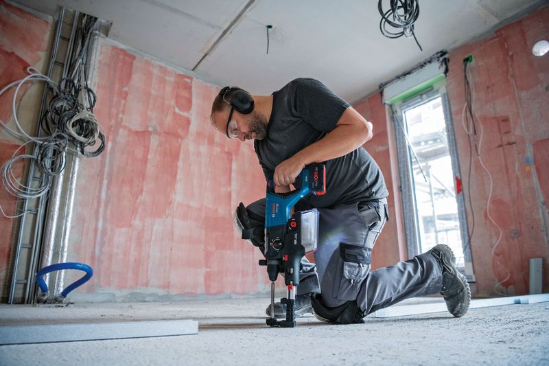 บุคคลที่สวมอุปกรณ์ด้านความปลอดภัยกำลังเจาะลงไปในพื้นคอนกรีตด้วยสว่านโรตารี่ไร้สาย.