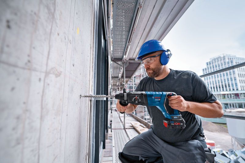 บุคคลที่สวมอุปกรณ์ด้านความปลอดภัยกำลังเจาะเข้าไปในผนังคอนกรีตด้วยค้อนโรตารี่.