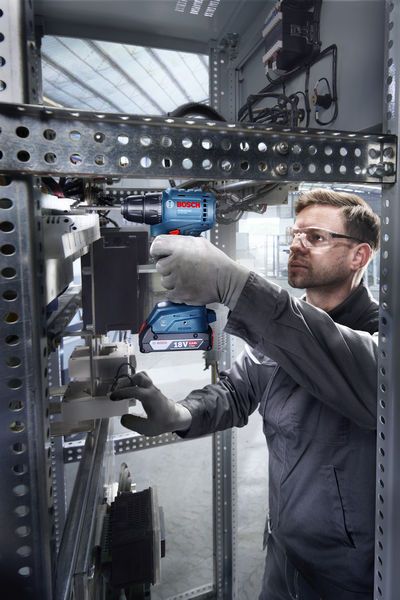 บุคคลที่สวมอุปกรณ์ด้านความปลอดภัยใช้สว่านไร้สายภายในตู้ไฟฟ้า.