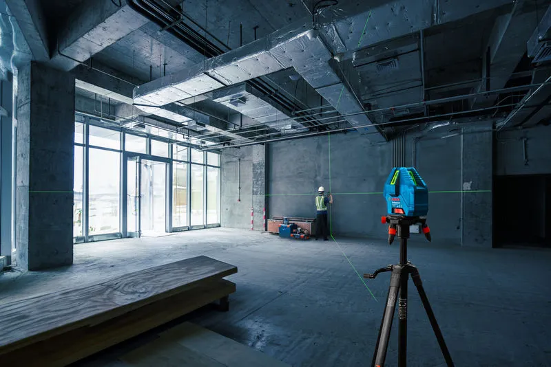 บุคคลที่สวมอุปกรณ์ด้านความปลอดภัยกำลังปรับระดับผนังโดยใช้เครื่องมือวัดระดับเลเซอร์ในสถานที่ก่อสร้าง.