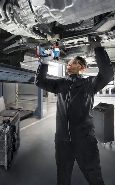 ผู้ที่สวมอุปกรณ์ด้านความปลอดภัยใช้สว่านไร้สายใต้รถที่ยกสูง.