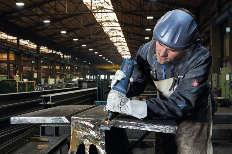 บุคคลที่สวมอุปกรณ์ด้านความปลอดภัยใช้เครื่องเจียรตรงกับคานโลหะ.