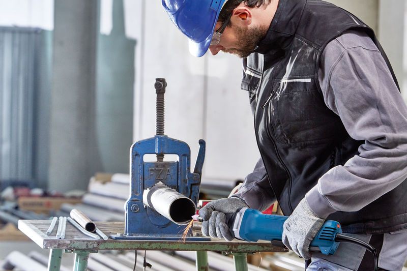 บุคคลที่สวมอุปกรณ์ด้านความปลอดภัยใช้เครื่องเจียรตรงในการทำงานกับท่อโลหะ.