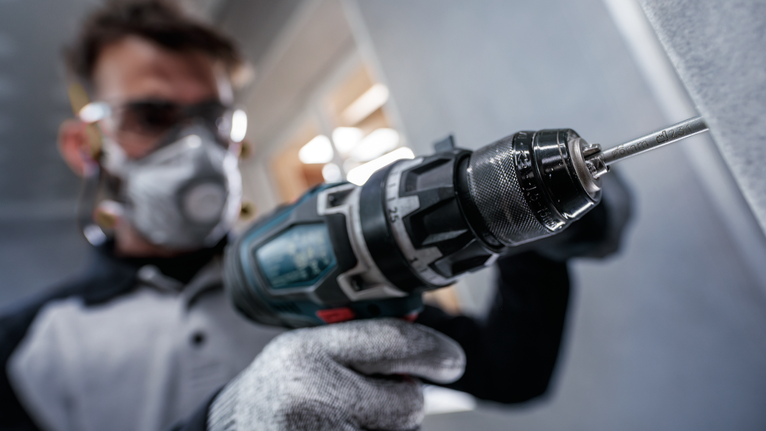 บุคคลที่สวมอุปกรณ์ความปลอดภัยเจาะเข้าไปในผนังด้วยเครื่องมือไฟฟ้า