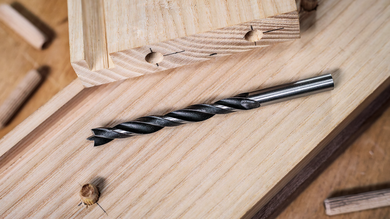 วางดอกสว่านไว้บนแผ่นไม้โดยมีเดือยวางอยู่ใกล้ๆ