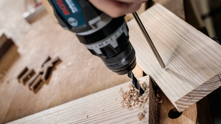 คนกำลังเจาะรูบนแผ่นไม้บนโต๊ะทำงาน