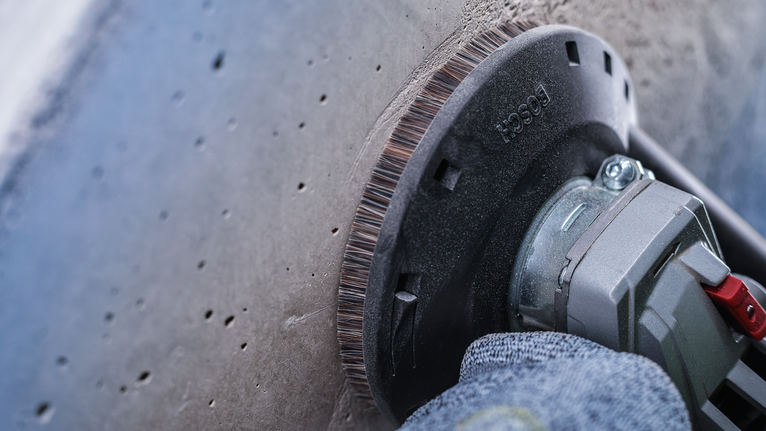 คนงานที่สวมอุปกรณ์ด้านความปลอดภัยกำลังขัดพื้นคอนกรีตด้วยเครื่องมือไฟฟ้า.