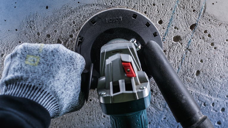 คนงานสวมอุปกรณ์ความปลอดภัยกำลังบดผนังคอนกรีตด้วยเครื่องมือไฟฟ้า.