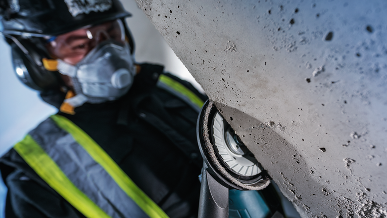 บุคคลที่สวมอุปกรณ์ด้านความปลอดภัยกำลังขัดพื้นคอนกรีตด้วยเครื่องมือไฟฟ้า.