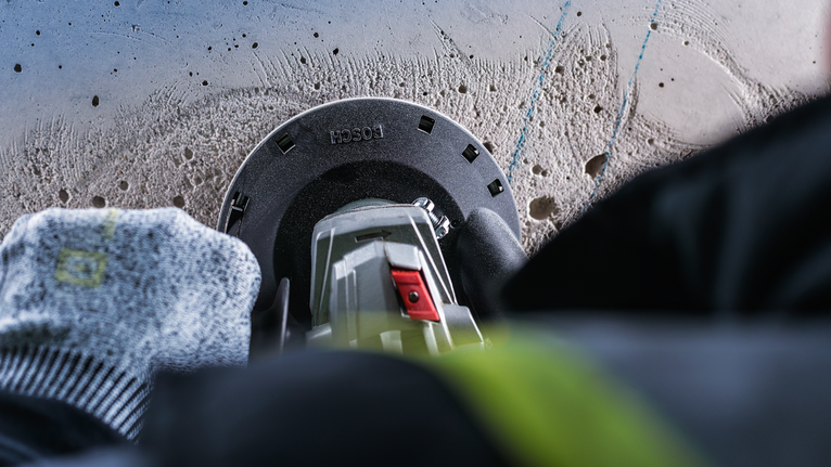 คนงานที่สวมอุปกรณ์ป้องกันความปลอดภัยกำลังเจาะเข้าไปในคอนกรีตโดยใช้เครื่องมือไฟฟ้า.