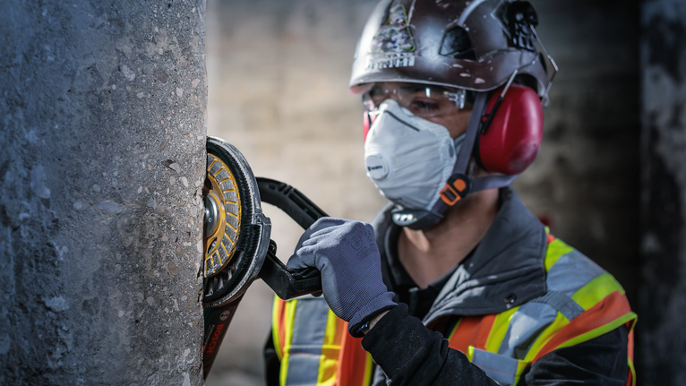 บุคคลที่สวมอุปกรณ์ความปลอดภัยกำลังบดเสาคอนกรีตด้วยเครื่องมือไฟฟ้า