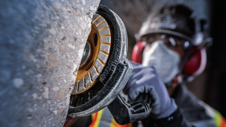 บุคคลที่สวมอุปกรณ์ความปลอดภัยกำลังเจียรผนังคอนกรีตด้วยเครื่องมือไฟฟ้า