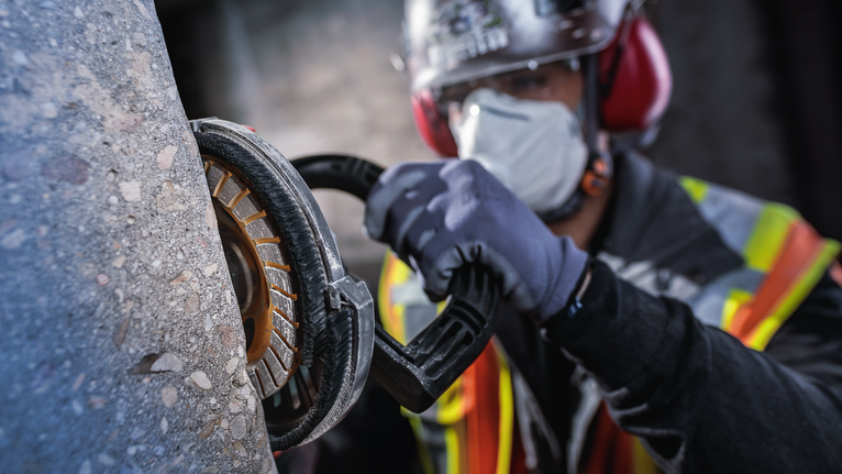 บุคคลที่สวมอุปกรณ์ความปลอดภัยกำลังบดคอนกรีตด้วยเครื่องมือไฟฟ้า