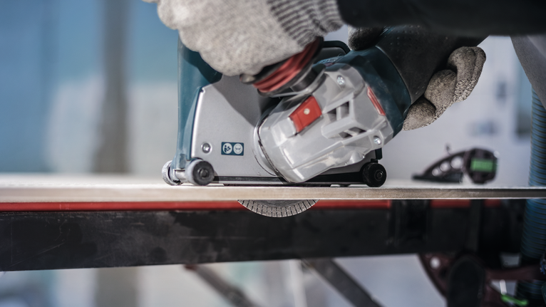 บุคคลที่สวมอุปกรณ์ความปลอดภัยกำลังใช้งานเครื่องมือไฟฟ้าเพื่อตัดกระเบื้อง