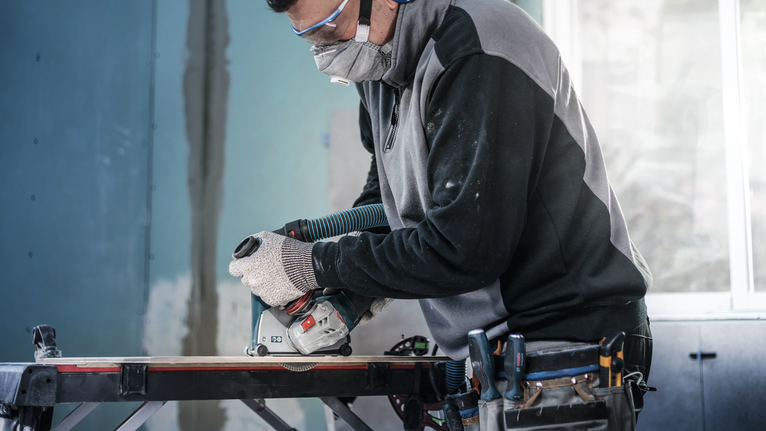 บุคคลที่สวมอุปกรณ์ความปลอดภัยใช้เลื่อยวงเดือนตัดไม้บนโต๊ะทำงาน