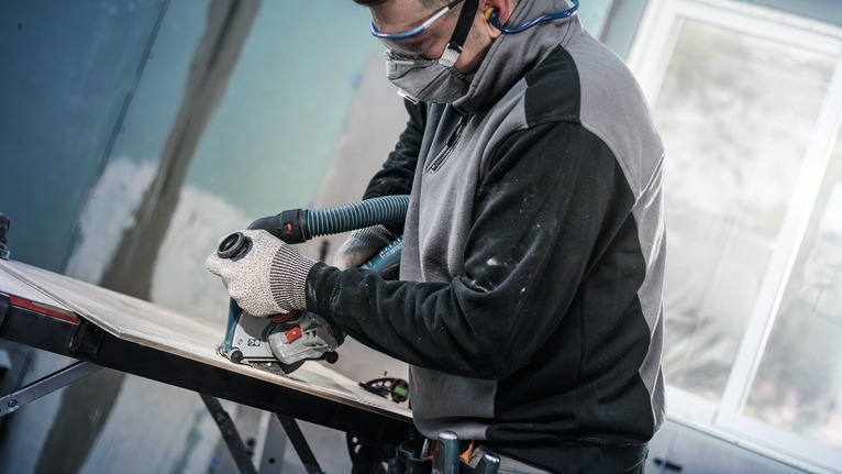 บุคคลที่สวมอุปกรณ์ด้านความปลอดภัยกำลังตัดไม้โดยใช้เครื่องมือไฟฟ้าที่ต่อกับท่อสูญญากาศ