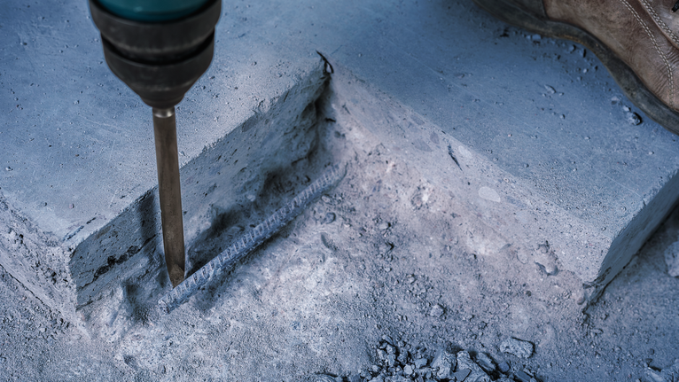 บุคคลที่สวมอุปกรณ์ความปลอดภัยใช้เครื่องมือรื้อถอนเพื่อทุบคอนกรีต