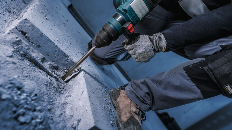 บุคคลที่สวมอุปกรณ์ความปลอดภัยกำลังเจาะเข้าไปในคอนกรีตด้วยค้อนโรตารี่