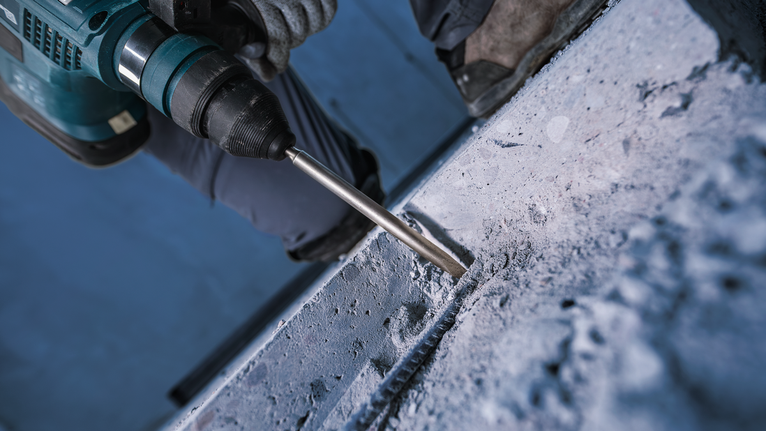 บุคคลที่สวมอุปกรณ์ความปลอดภัยกำลังเจาะเข้าไปในคอนกรีตด้วยค้อนโรตารี่