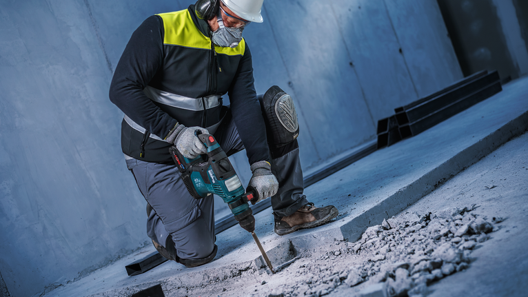 บุคคลที่สวมอุปกรณ์ด้านความปลอดภัยใช้ค้อนโรตารี่เพื่อทุบคอนกรีต