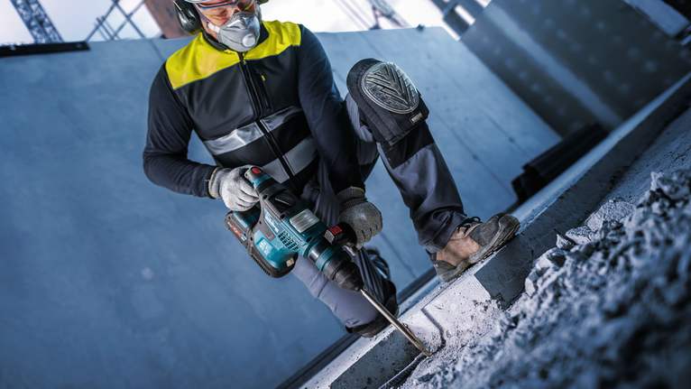 บุคคลที่สวมอุปกรณ์ความปลอดภัยกำลังเจาะเข้าไปในคอนกรีตด้วยค้อนโรตารี่