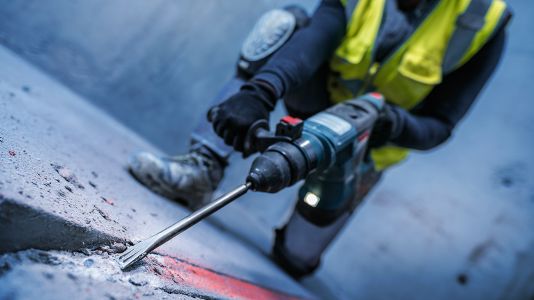 บุคคลที่สวมอุปกรณ์ด้านความปลอดภัยกำลังสกัดพื้นคอนกรีตด้วยค้อนโรตารี่