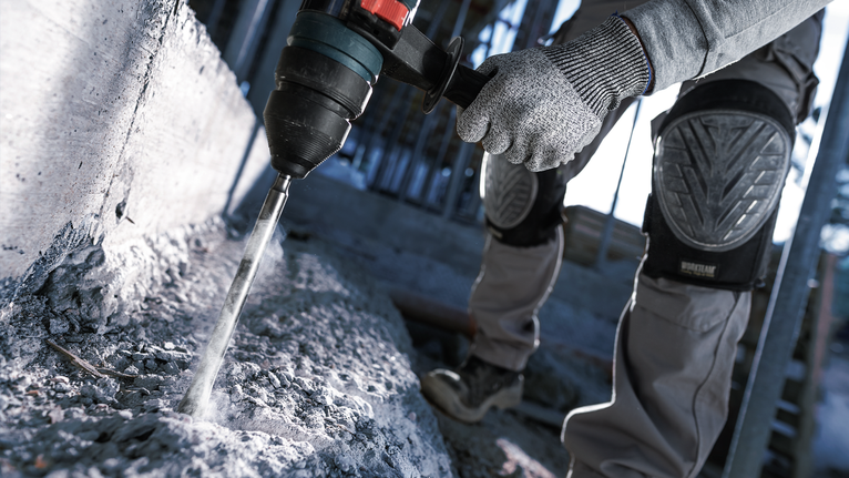 บุคคลที่สวมอุปกรณ์ความปลอดภัยกำลังเจาะเข้าไปในคอนกรีตด้วยค้อนโรตารี่