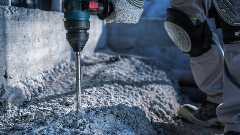 บุคคลที่สวมอุปกรณ์ความปลอดภัยกำลังเจาะเข้าไปในคอนกรีตที่ไซต์ก่อสร้าง