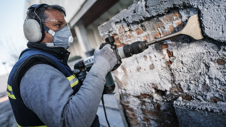 บุคคลที่สวมอุปกรณ์ด้านความปลอดภัยกำลังถอดคอนกรีตออกจากผนังโดยใช้เครื่องมือรื้อถอน