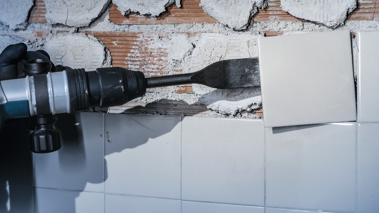 บุคคลที่สวมอุปกรณ์ด้านความปลอดภัยใช้เครื่องมือไฟฟ้าในการถอดกระเบื้องผนัง