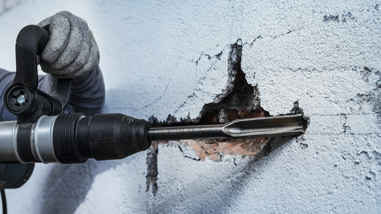 บุคคลที่สวมอุปกรณ์ด้านความปลอดภัยใช้ค้อนโรตารี่สกัดเข้าไปในผนัง