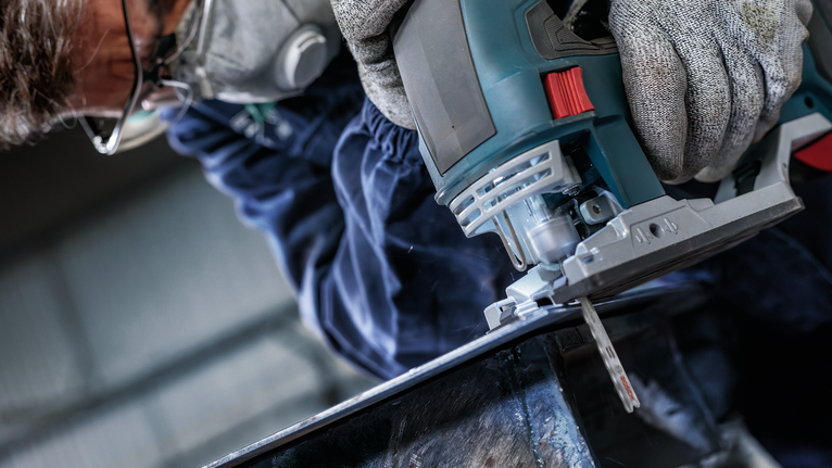 ผู้ที่สวมอุปกรณ์ความปลอดภัยใช้จิ๊กซอว์ตัดผ่านโลหะ