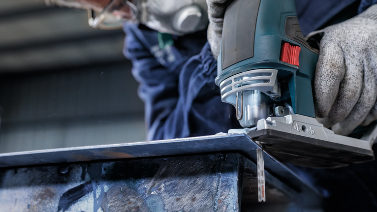 ผู้ที่สวมอุปกรณ์ความปลอดภัยใช้จิ๊กซอว์ตัดผ่านแผ่นโลหะ