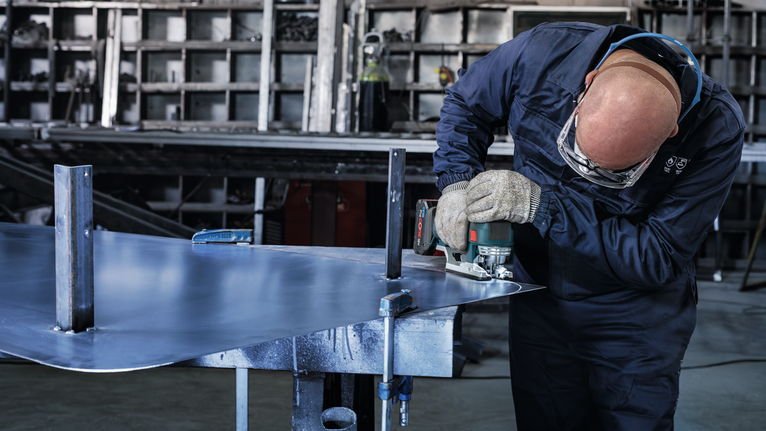 บุคคลที่สวมอุปกรณ์ความปลอดภัยกำลังตัดแผ่นโลหะด้วยเครื่องมือไฟฟ้า