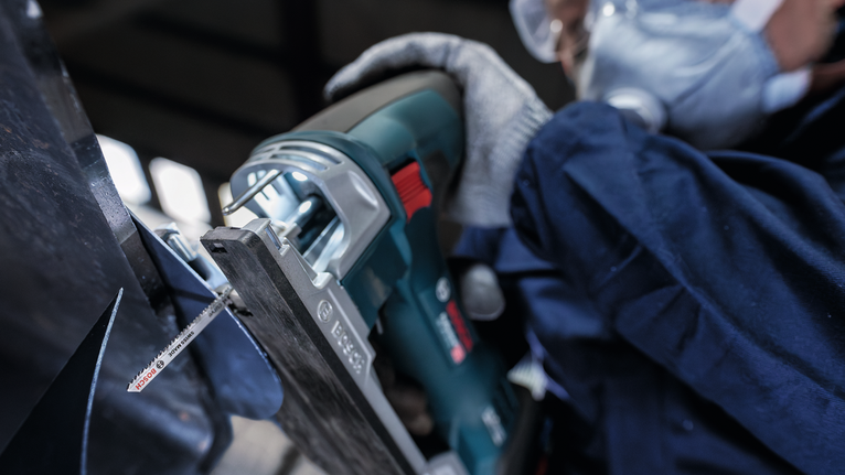 บุคคลที่สวมอุปกรณ์ความปลอดภัยกำลังตัดโลหะด้วยเลื่อยตัดโลหะ