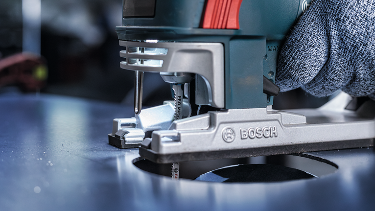 บุคคลที่สวมอุปกรณ์ความปลอดภัยกำลังนำจิ๊กซอว์ไปตัดรูวงกลมในโลหะ