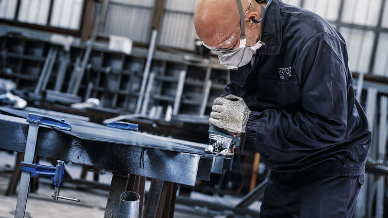 บุคคลที่สวมอุปกรณ์ความปลอดภัยใช้เลื่อยไฟฟ้าตัดโลหะในโรงงาน