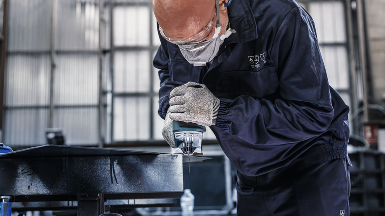 บุคคลที่สวมอุปกรณ์ความปลอดภัยกำลังตัดโลหะโดยใช้เลื่อยไฟฟ้ามือถือ