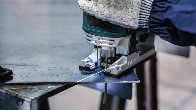 บุคคลที่สวมอุปกรณ์ความปลอดภัยกำลังตัดแผ่นโลหะด้วยจิ๊กซอว์