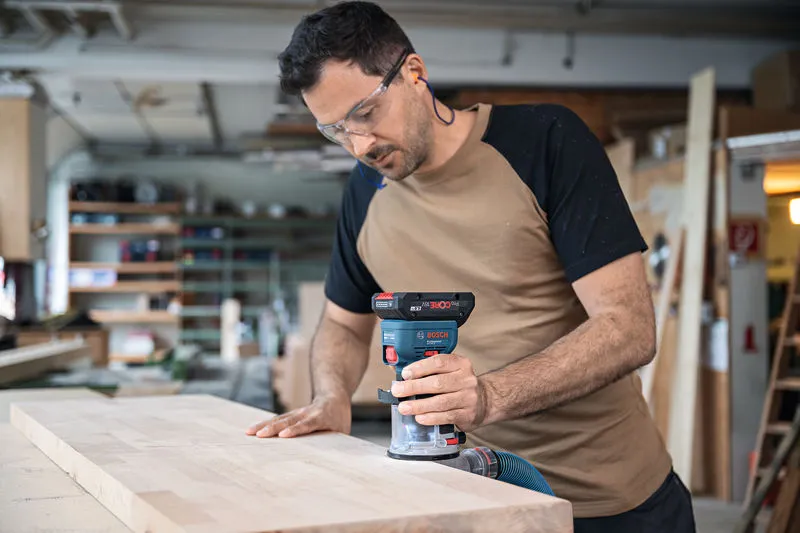 บุคคลที่สวมอุปกรณ์ป้องกันความปลอดภัยกำลังตัดขอบแผ่นไม้ด้วยเครื่องเราเตอร์ไร้สาย.